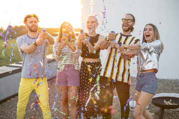 Young stylish friends have fun, shooting confetti during some celebration at rooftop terrace on a sunset