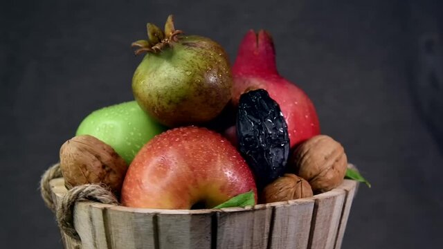 Close-up of wooden basket with apples,  walnuts, dates and pomegranates are sweet symbols of Jewish New Year - Rosh Hashanah, blurred gray background 