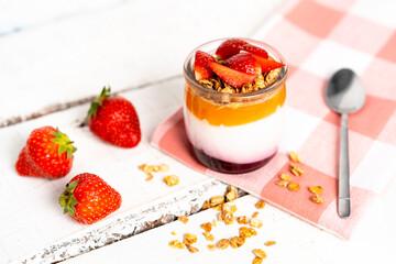 Fruit yogurt berry with muesli and fresh strawberries, on a white wooden background