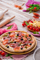 Juicy pizza with sausages, tomatoes and olives on a white wooden background. Space for text. High quality photo