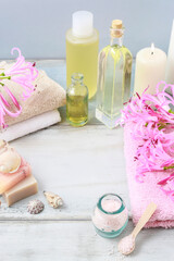 Spa set: bottle of essential oil, liquid soap, scoop of raspberry sea salt, towels and pink hyacinth flowers