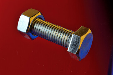 new, chrome-plated bolts and nuts on a red background.