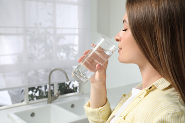 Woman drinking tap water from glass in kitchen