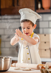 Toddler boy playing with the dough in the kitchen dressed as a chef. Child baking a cake