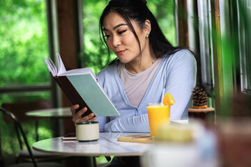 Young Asian woman sitting in coffee shop and reading book.	