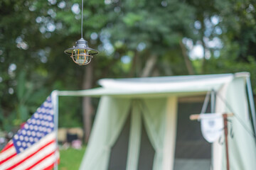 a vintage hanging black camping lantern with blurred background of tents and American flag in the camping area at natural