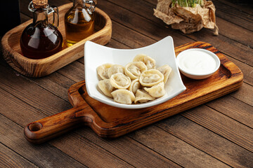 Russian pelmenii dumplings with sour cream on wooden background