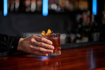 Barman holding out glass with alcoholic cocktail to the client