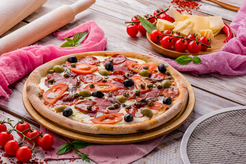 Juicy pizza with sausages, tomatoes and olives on a white wooden background. Space for text. High quality photo