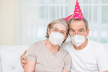 Portrait of a happy senior couple wearing party's caps and protective masks celebrate birthday together during the coronavirus epidemic