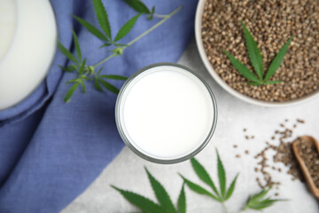 Hemp milk and seeds with fresh leaves on light grey table, flat lay