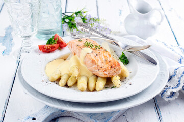 Traditional Altantic fried salmon filet white asparagus in sauce hollandaise and tomatoes served as close-up on a classic design plate