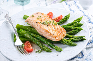 Traditional fried salmon filet with green asparagus and tomatoes served as close-up on a classic design plate
