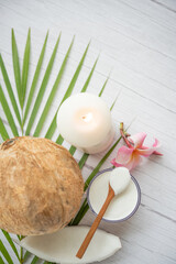 Coconut oil, tropical leaves and fresh coconuts. Spa coconut products on light wooden background. Spa still life of organic cosmetics with coconuts on a light wooden background, body care concept.