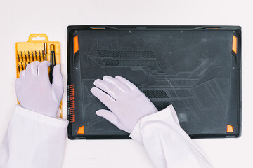 View from above of a white gloved hands of an engineer, picking up a screwdriver to open the lid of...
