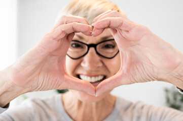 An elderly woman with eyeglasses showing heart sign