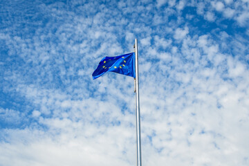 European Union flag blowing in the wind towards cloudy blue sky in a sunny sprng day.