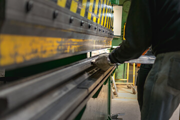Workers handling piece of metal sheet into a folding machine