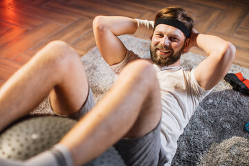 Close up of likable happy smiling sporty man lying on floor and doing crunches for abdominal...