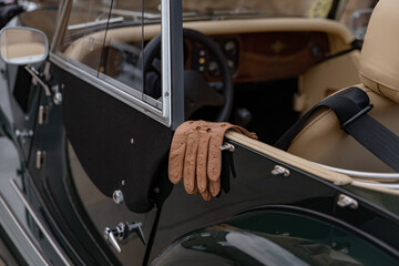Naklejka premium Driver's leather gloves hang on the body of a vintage car