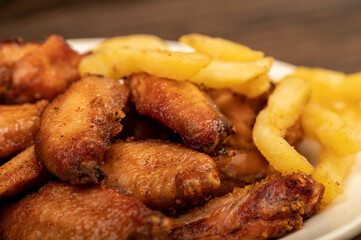 Fried chicken wings and French fries on a plate, close-up, selective focus.
