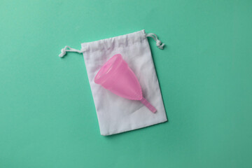 Menstrual cup with cotton bag on turquoise background, top view