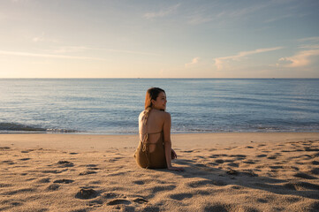 Young asian woman in swimwear sitting and sunbathing on the beach in the morning