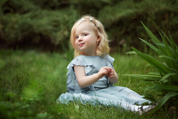 a little girl in a blue dress is sitting on the grass in the park in summer