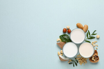 Vegan milk and different nuts on light background, flat lay. Space for text