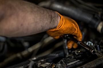 Obraz na płótnie Canvas A man wearing an orange glove fixing and doing maintenace on a car engine in an auto repair shop