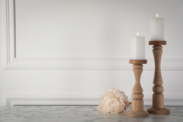 Elegant candlesticks with burning candles and flower on white marble table. Space for text
