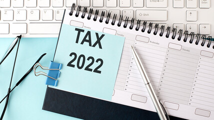 TAX 2022 text on blue sticker on planning and keyboard,blue background