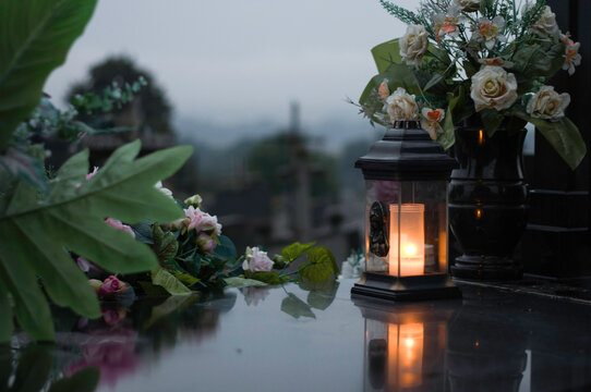 The lantern with candle and flowers as a decoration on the marble grave and cemetery in the background.