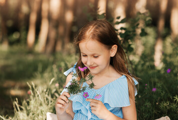 Beautiful little girl in a blue dress with flowers in nature in the summer