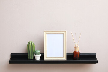 Empty photo frame, cactus figures and air reed freshener on shelf near pink wall