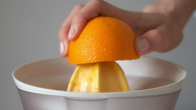 Woman is squeezing oranges using electric juicer in the kitchen, hand closeup. Healthy vegan ripe fruit juice, natural vitamins from food. Making orange juice pressing half of orange.