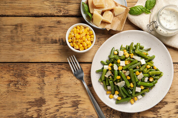Delicious salad with green beans, corn and cheese served on wooden table, flat lay. Space for text