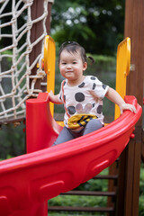 Two Year Old Asian Baby Girl Playing on a Red Slider on the Playground