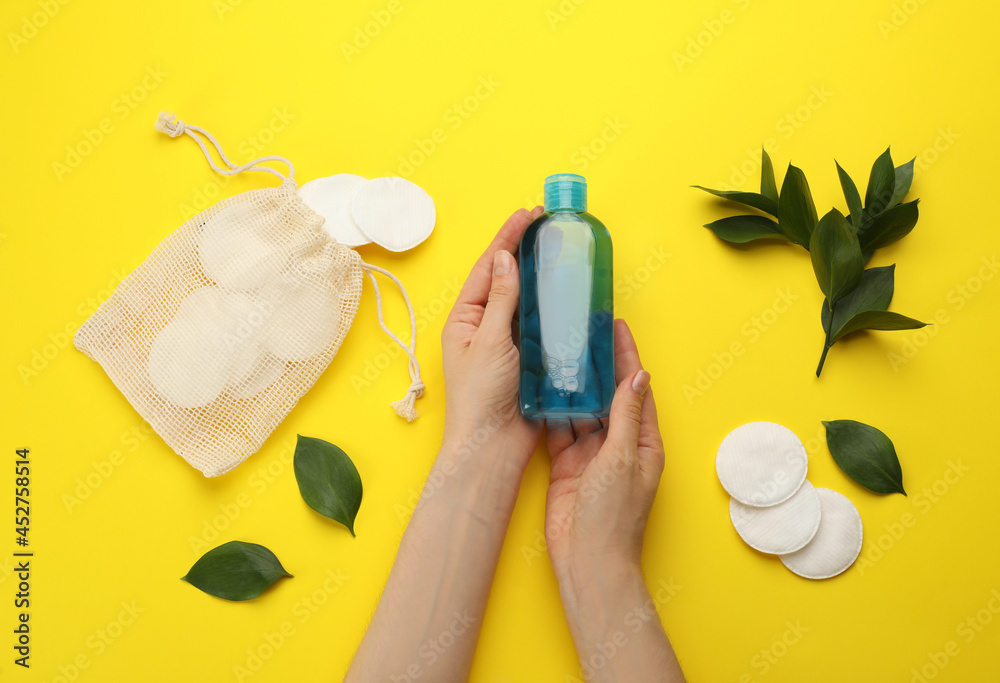 Wall mural Woman holding makeup removal product on yellow  background, top view