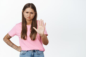 Stop. Young woman frowning and showing raised palm, saying no, refusing, declining bad offer,...