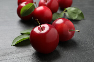 Delicious ripe cherry plums with leaves on black table, closeup