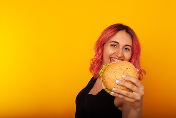 a woman with bright pink hair shows a delicious burger with a smile on her face charming. Advertising fast food, I love junk food. vs vegans. Vegan Burger Without Meat. space for text