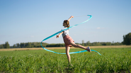 Young girl in the field with a blue gymnastic ribbon