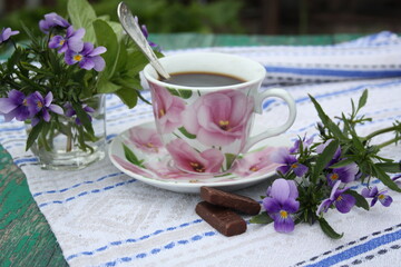 Breakfast in nature. A cup of coffee, chocolates and flowers on a beautiful napkin. There is room for text.
