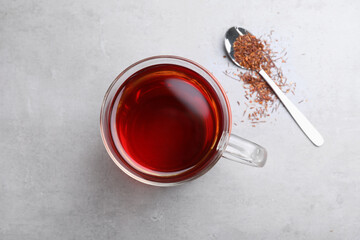 Freshly brewed rooibos tea, scattered dry leaves and spoon on grey table, flat lay