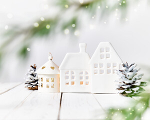 White Christmas composition with candle holders in the shape of a house, fir branches and Christmas lights. Home decor for winter holidays, postcard template, happy new year and marry christmas.