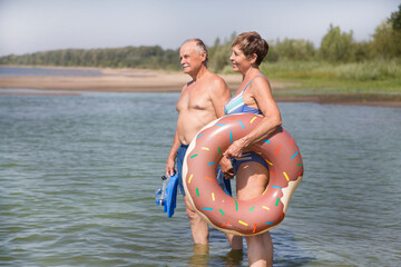 Happy senior  couple alk on the beach with inflatable rings on a sunny day
 - Powered by Adobe