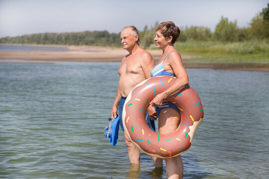 Happy senior  couple alk on the beach with inflatable rings on a sunny day
