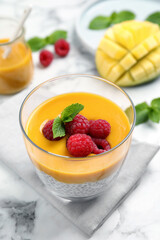 Delicious chia pudding with mango sauce and raspberries on white marble table