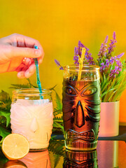 Vertical shot of a hand mixing cocktail with a straw in a fancy glass with a tiki face